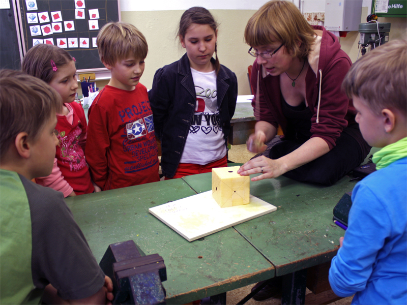 Holzgestalterin Julia Franke erläutert den Grundschülern im Werkraum der Schule, welche Kristallformen in einem Würfel versteckt sind. Foto: Ralph Sontag
